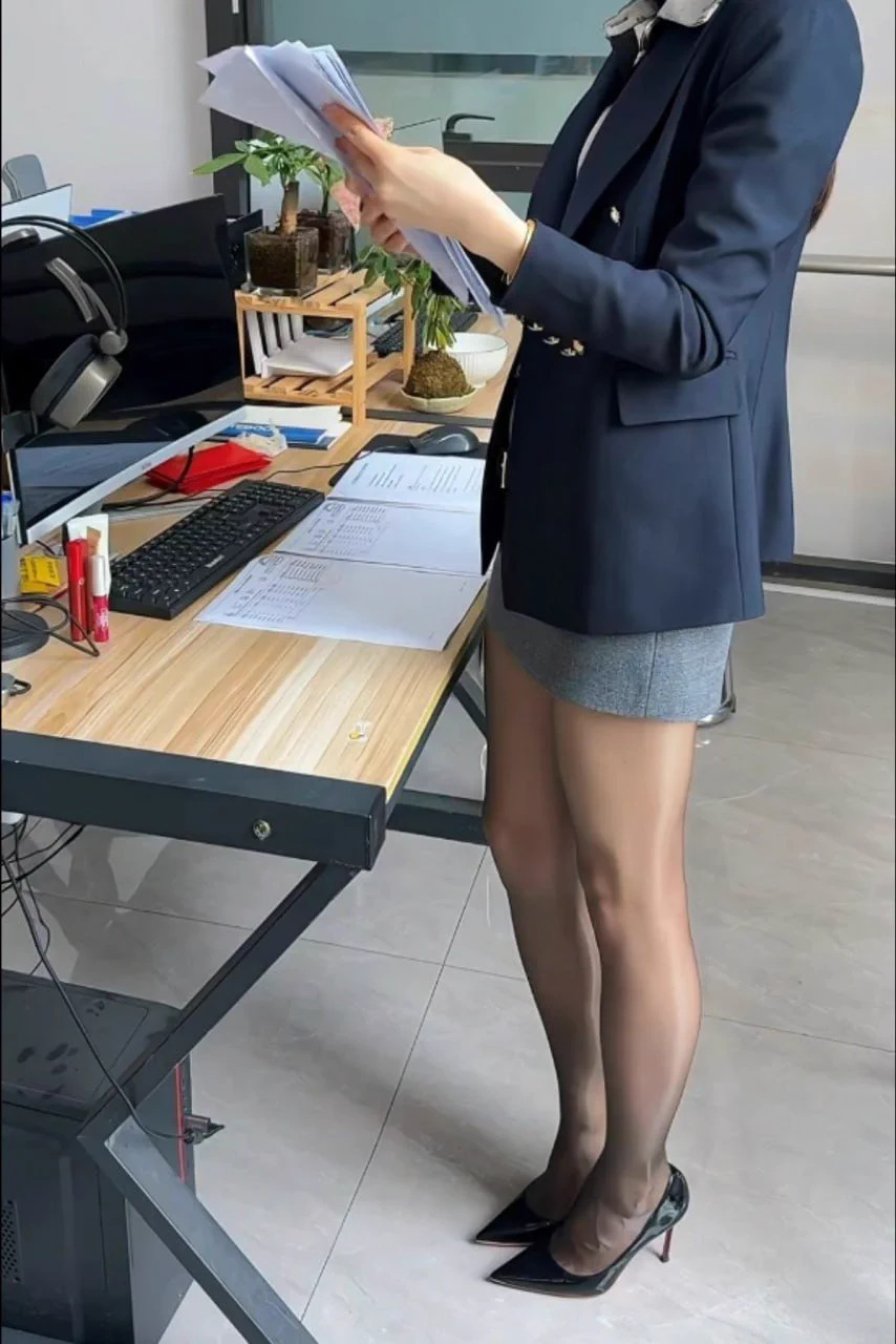 我站在办公桌前，手持文件，专注工作。深蓝色西装外套搭配灰色短裙，黑色高跟鞋和丝袜显出精致气质。专业又自信，这就是我的职场风采！ https://t.co/TQUmLWynSa